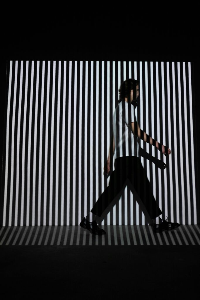 pexels-photo-6492178-6492178 A man walks in front of a black and white striped optical illusion background.
